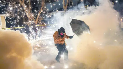 A person with an umbrella stands in a cloud of tear gas